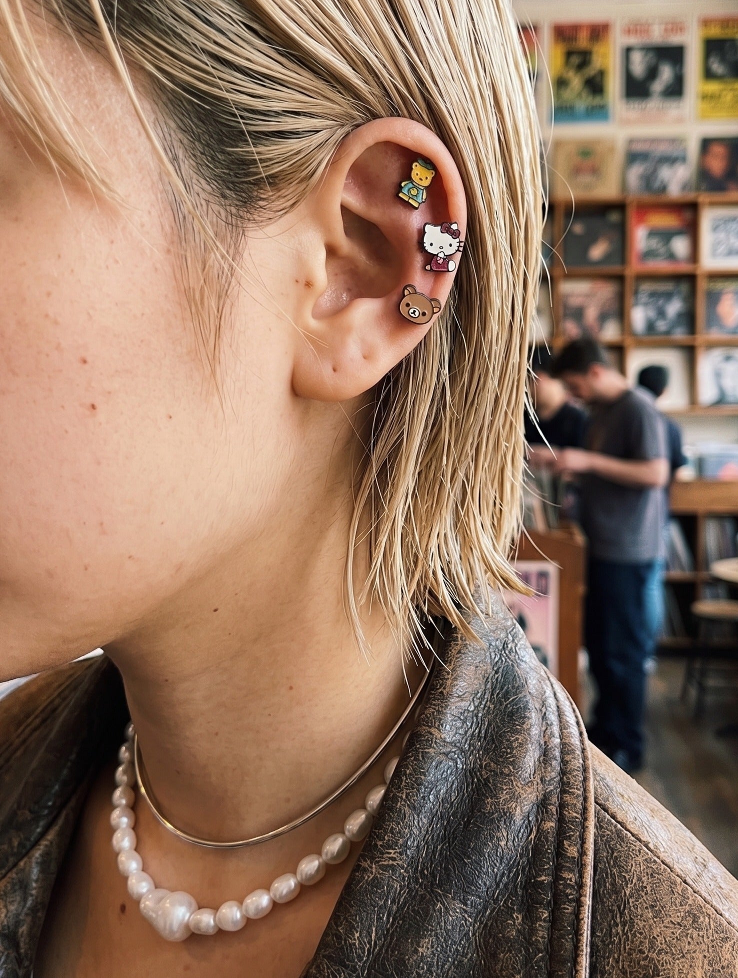 Kitsch aesthetic ear stack — Hello Kitty and Tiny Chum surgical steel character piercing studs on inner conch and helix, chunky pearl necklace, K-style curated ear