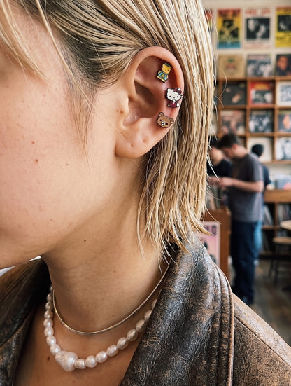 Kitsch aesthetic ear stack — Hello Kitty and Tiny Chum surgical steel character piercing studs on inner conch and helix, chunky pearl necklace, K-style curated ear