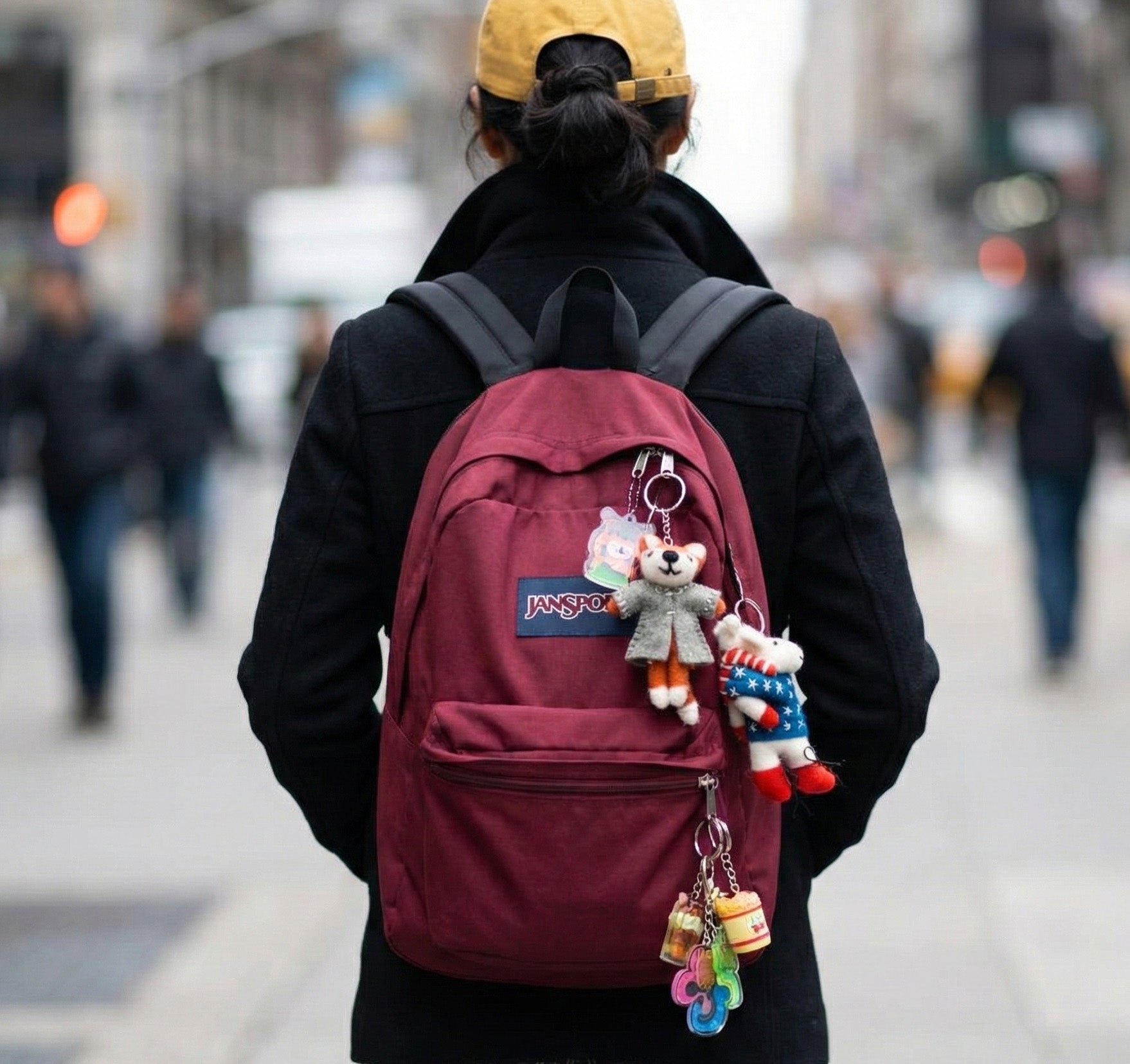Burgundy JanSport backpack with wool felt keychains viewed from behind on street