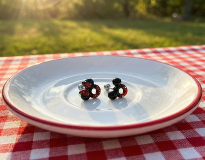Mickey and Minnie Mouse shaped barbell earrings displayed on a white plate in a sunlit outdoor picnic setting.