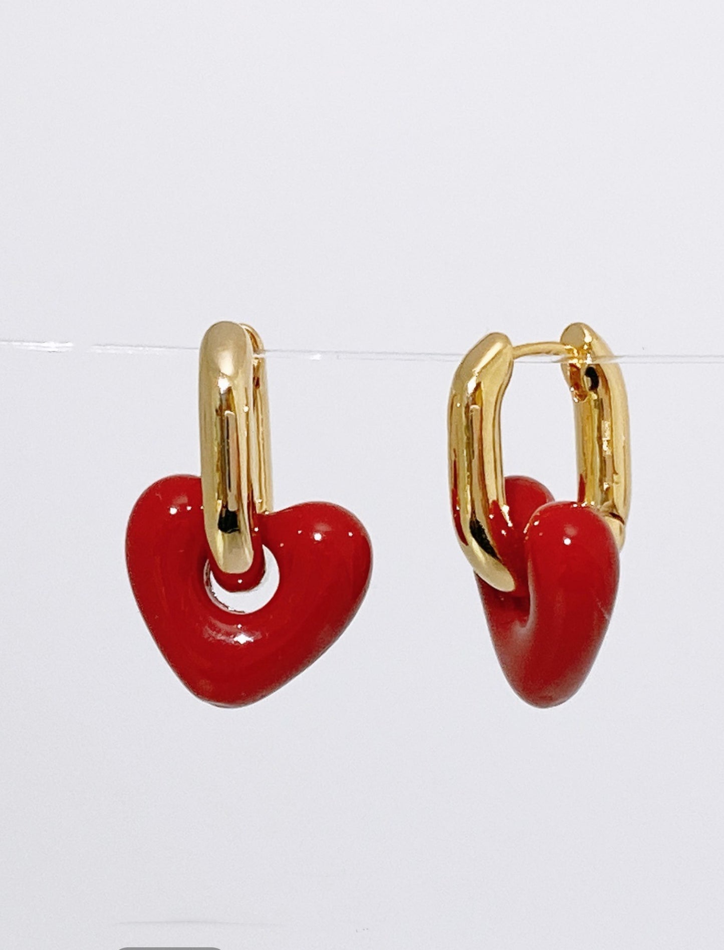 Close-up of red puffy heart charm drop earrings with gold-tone brass huggie hoops on white background