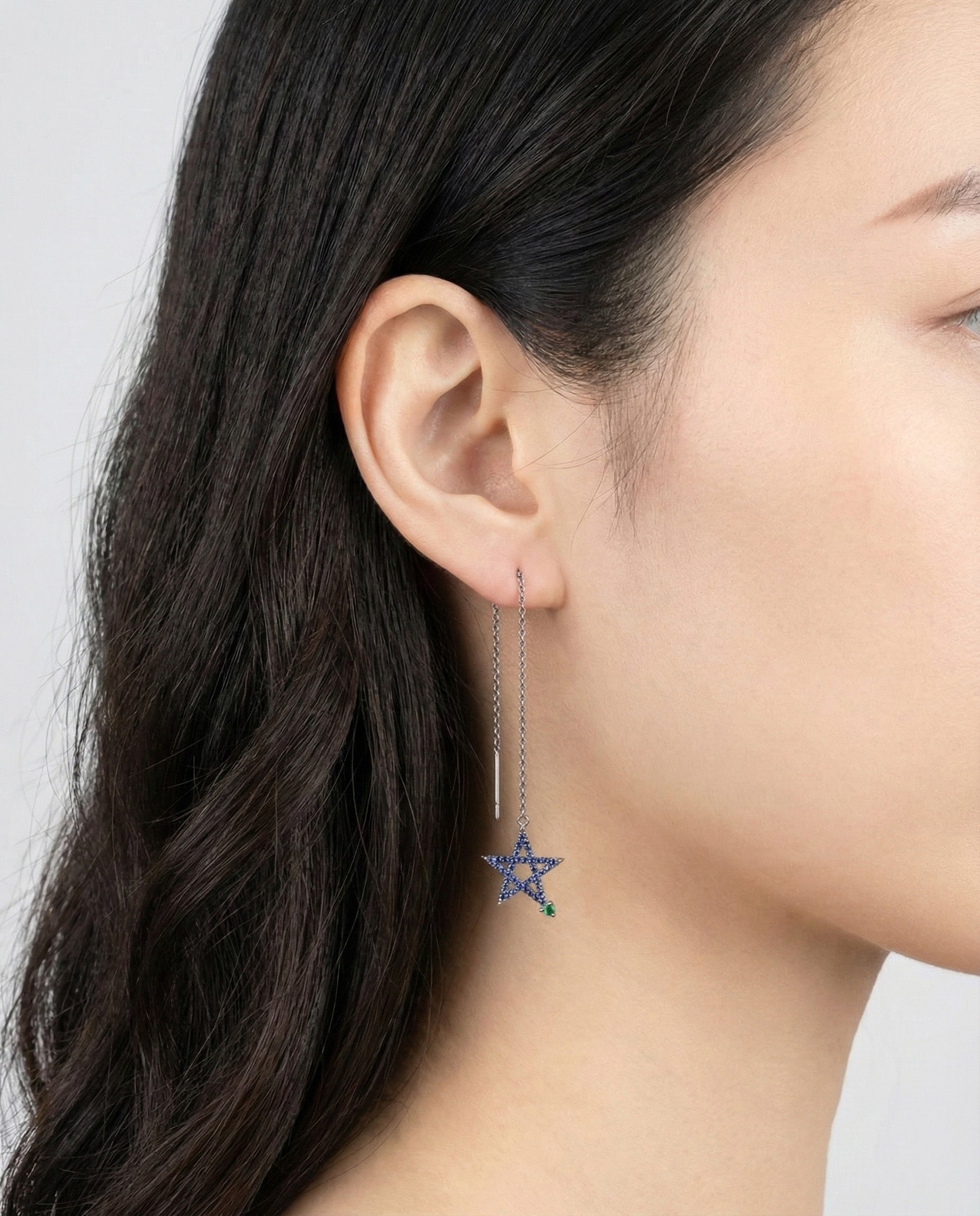 Close-up of deep blue pavé crystal star earring with emerald green accent on ear