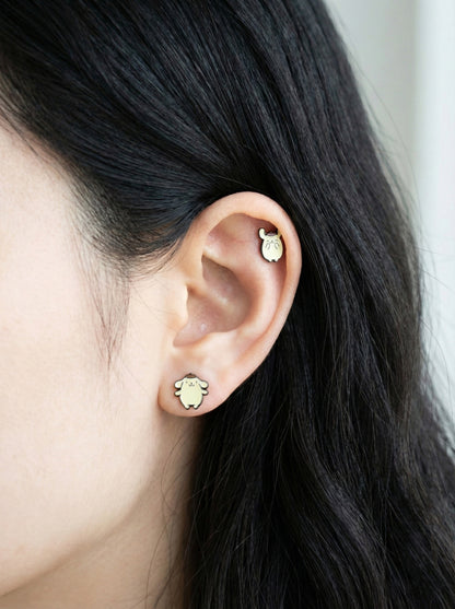 Close-up of Pompompurin brass piercings on earlobe and outer conch showing detailed enamel coloring