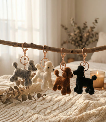Lifestyle shot of four wool felt poodle keychains hanging on natural wooden branch with cozy home interior background