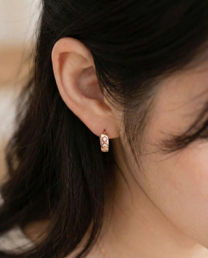 Front angle of rose gold hoop earring with star and cubic details worn on the right ear.
