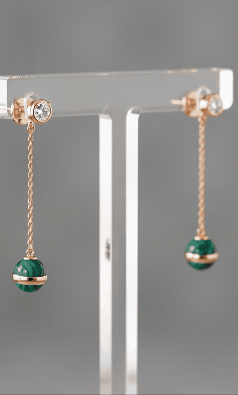 Animated loop of model wearing natural malachite rose gold drop earrings, showing chain movement and light reflection on deep green stone during motion