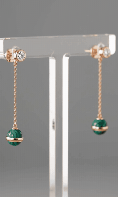 Animated loop of model wearing natural malachite rose gold drop earrings, showing chain movement and light reflection on deep green stone during motion