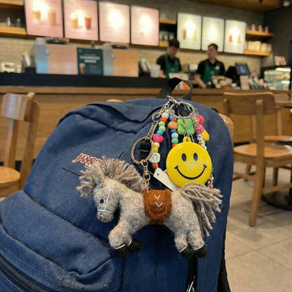 Grey wool felt horse bag charm attached to blue denim backpack at coffee shop