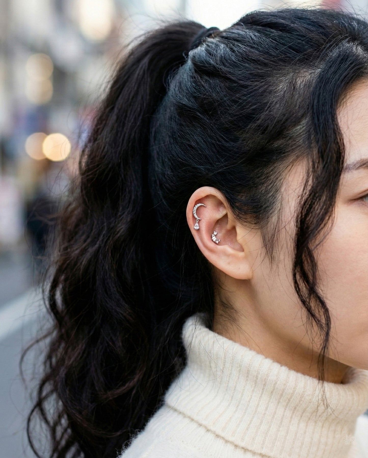 Side view of crescent moon surgical steel piercing on ear with white turtleneck sweater