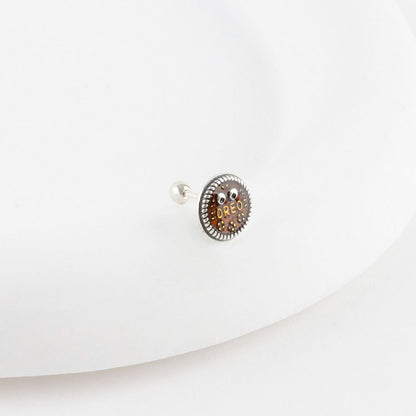 Close-up of brown Oreo cookie surgical steel stud piercing with 925 silver post, detailed texture and googly eyes on white background