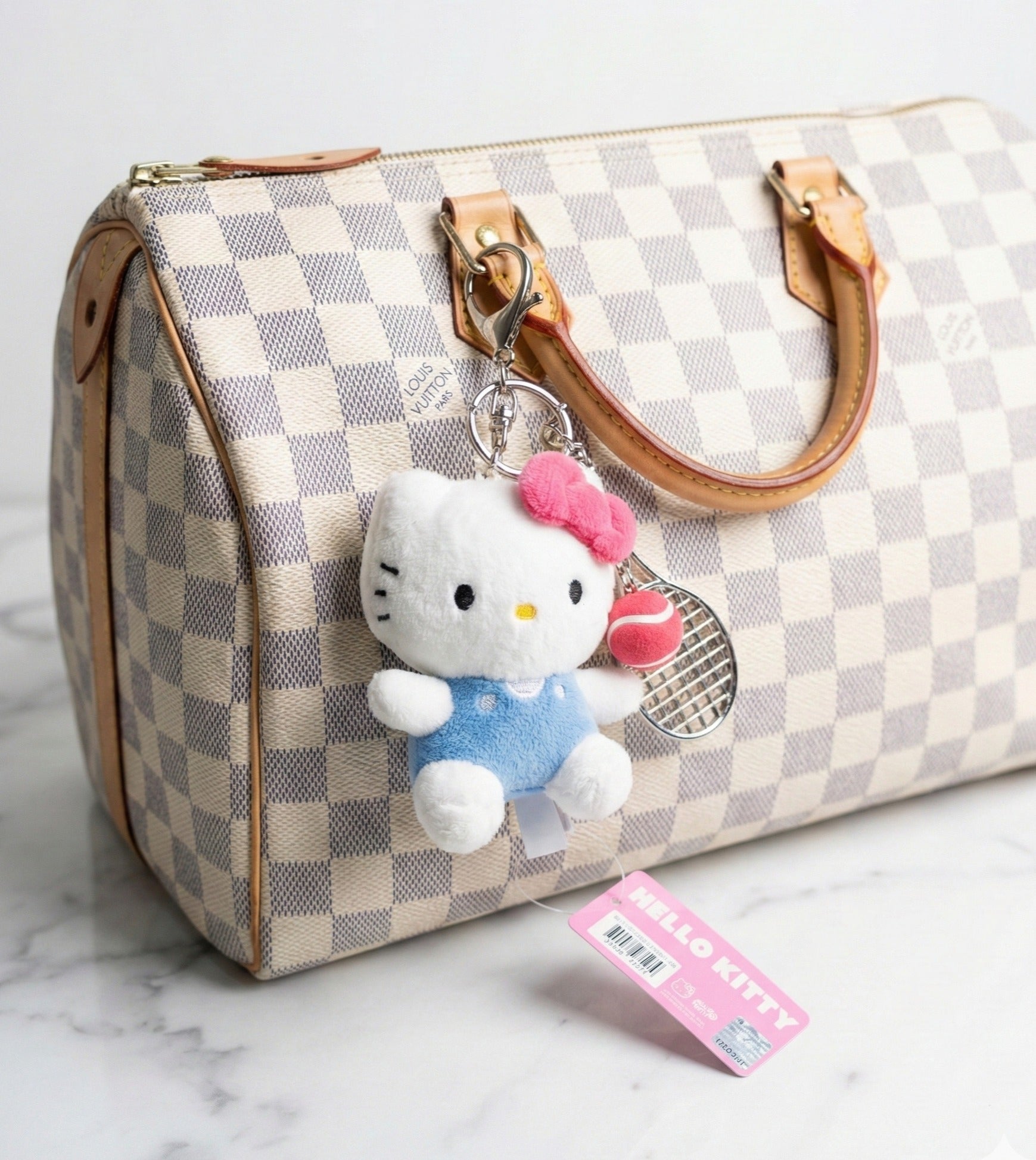Hello Kitty tennis bag charm attached to Louis Vuitton Damier Azur handbag — kawaii Y2K luxury bag accessory