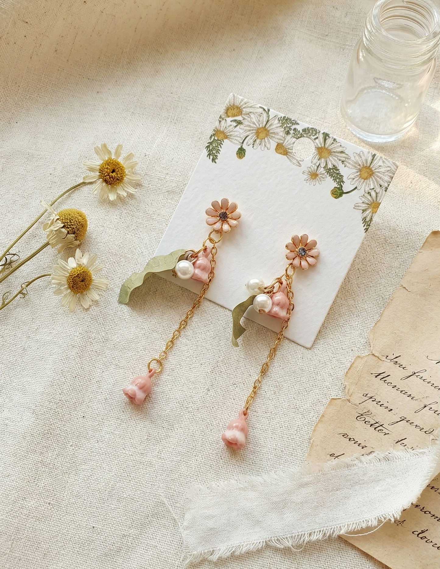 Close-up of pink flower drop earrings with pearls and green leaf charms.