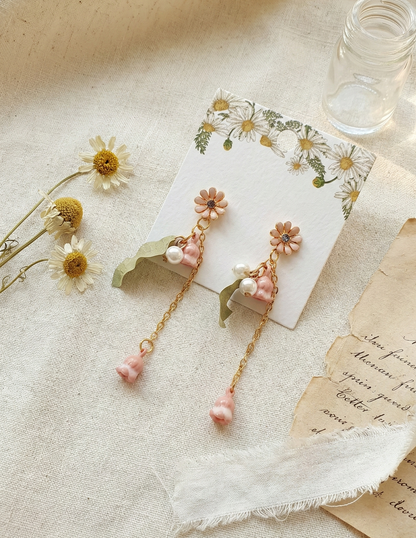 Close-up of pink flower drop earrings with pearls and green leaf charms.
