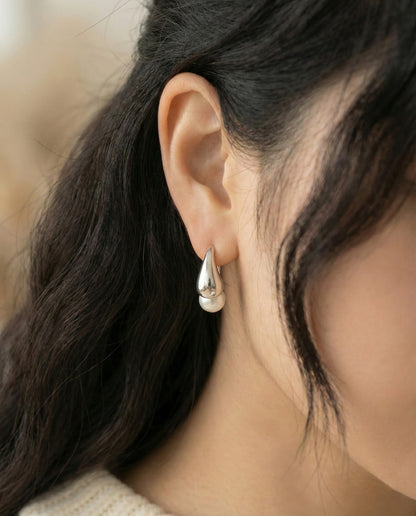 Close-up of silver teardrop pearl drop earring worn on ear showing sleek metal design