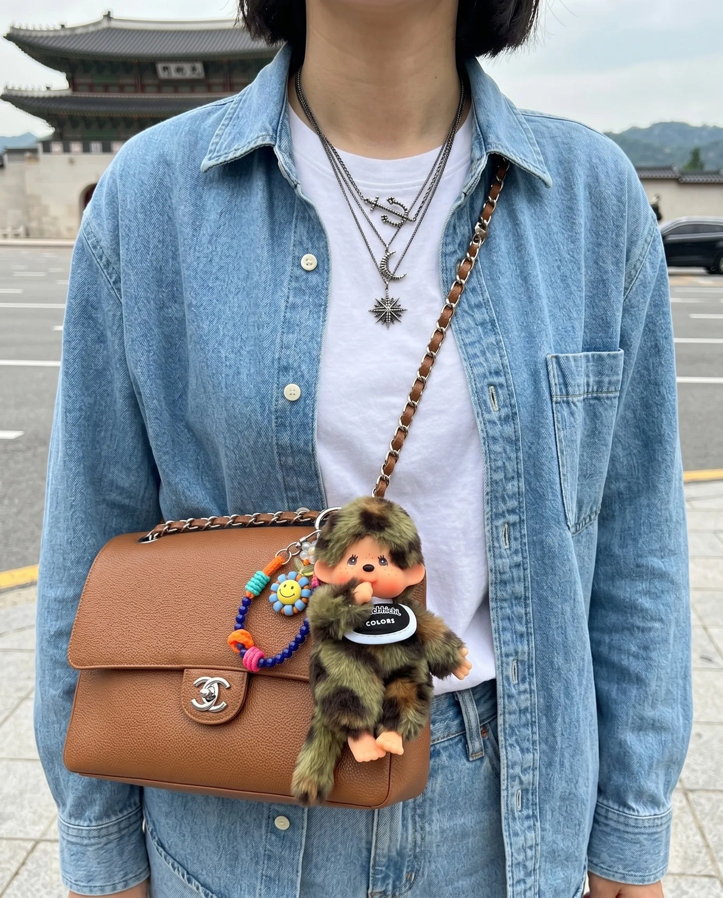 K-street style bag charm inspo with camo plush doll keychain 8ttitto8, layered with smiley bead strap on brown leather crossbody, downtown Seoul vibe.