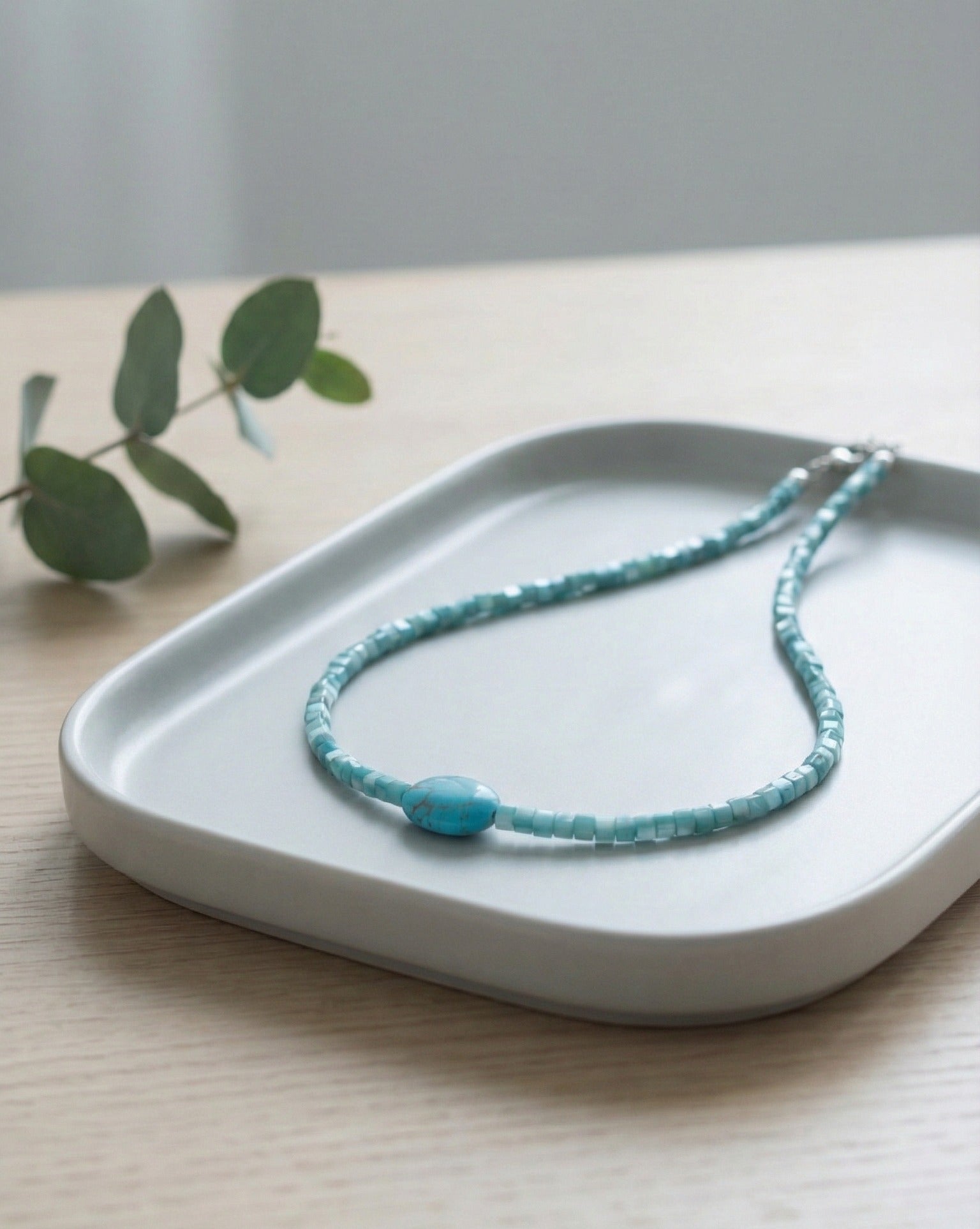 Turquoise gemstone choker with square shell beads on white ceramic tray