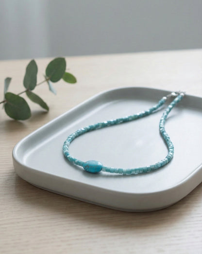 Turquoise gemstone choker with square shell beads on white ceramic tray