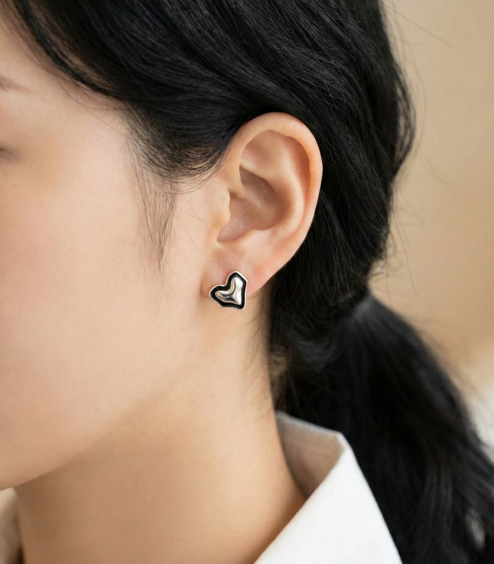 Woman wearing 925 sterling silver chunky puff heart stud earrings with black enamel border, white blouse, close-up side view