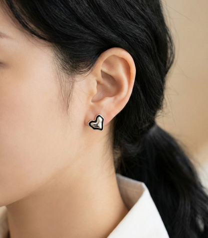 Woman wearing 925 sterling silver chunky puff heart stud earrings with black enamel border, white blouse, close-up side view