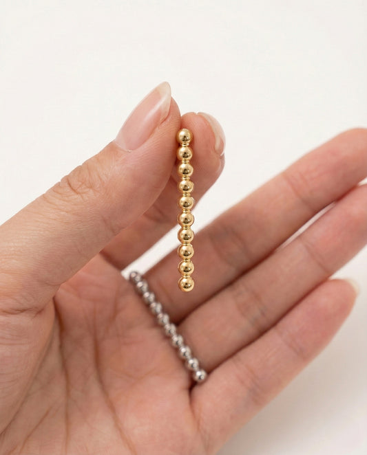 Close-up view of gold and silver ball drop earrings showing fixed linear design