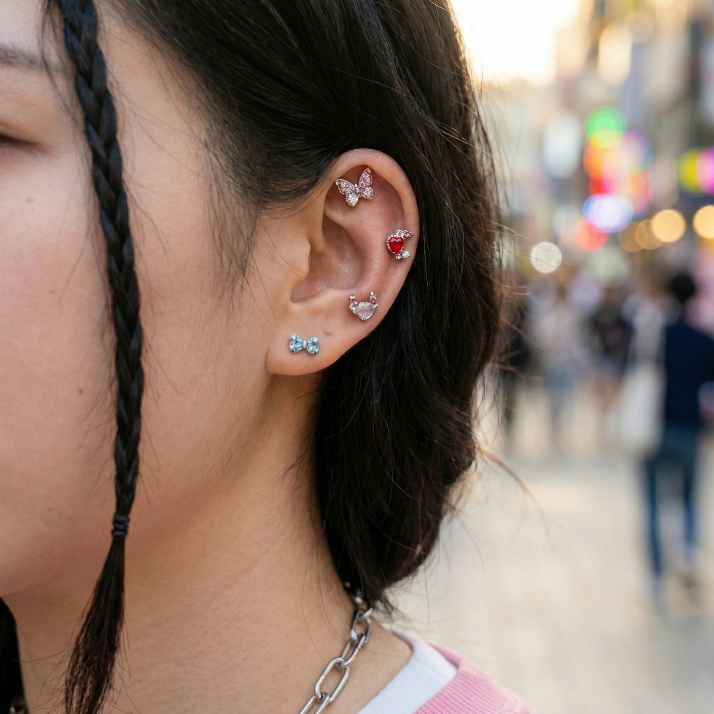 Woman wearing layered ear piercings including moon heart stud, butterfly cartilage earring, and ribbon bow stud on helix and conch