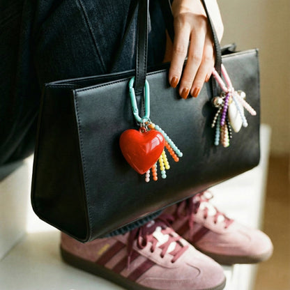Red heart bag charm with mint carabiner on black leather handbag with pink sneakers