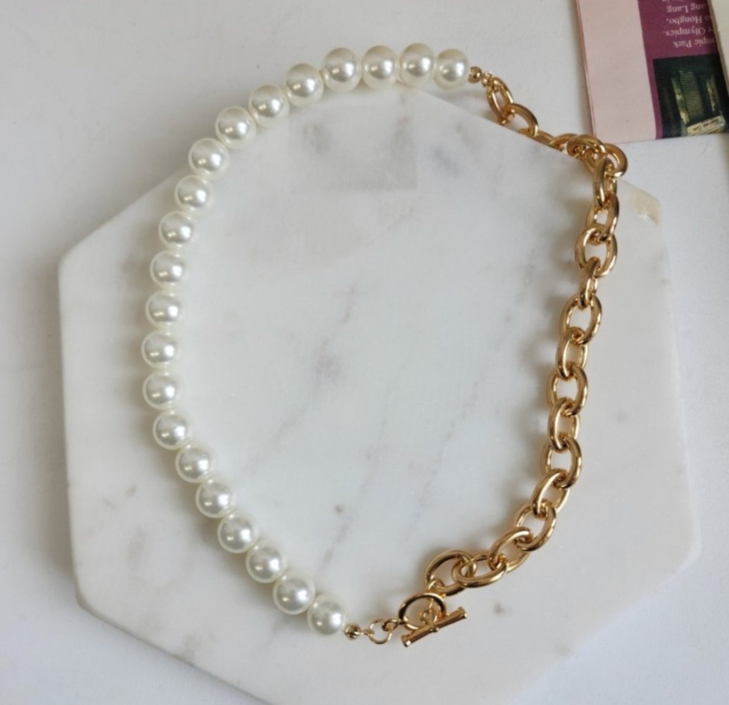 Overhead view of gold toggle choker with pearl and brass chain on white display