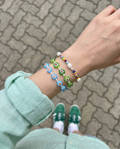 Layered wrist stack aesthetic — sky blue and apple green Millefiori flower bead bracelets with freshwater pearl bracelet, mint linen shirt look.
