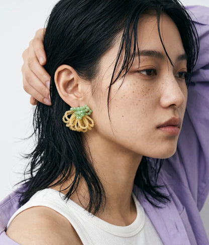 close-up portrait of a young woman showcasing premium K-beauty styling with dewy, naturally freckled skin and wet-look hair. She is wearing mint green and pale yellow beaded statement earrings and a lilac shirt