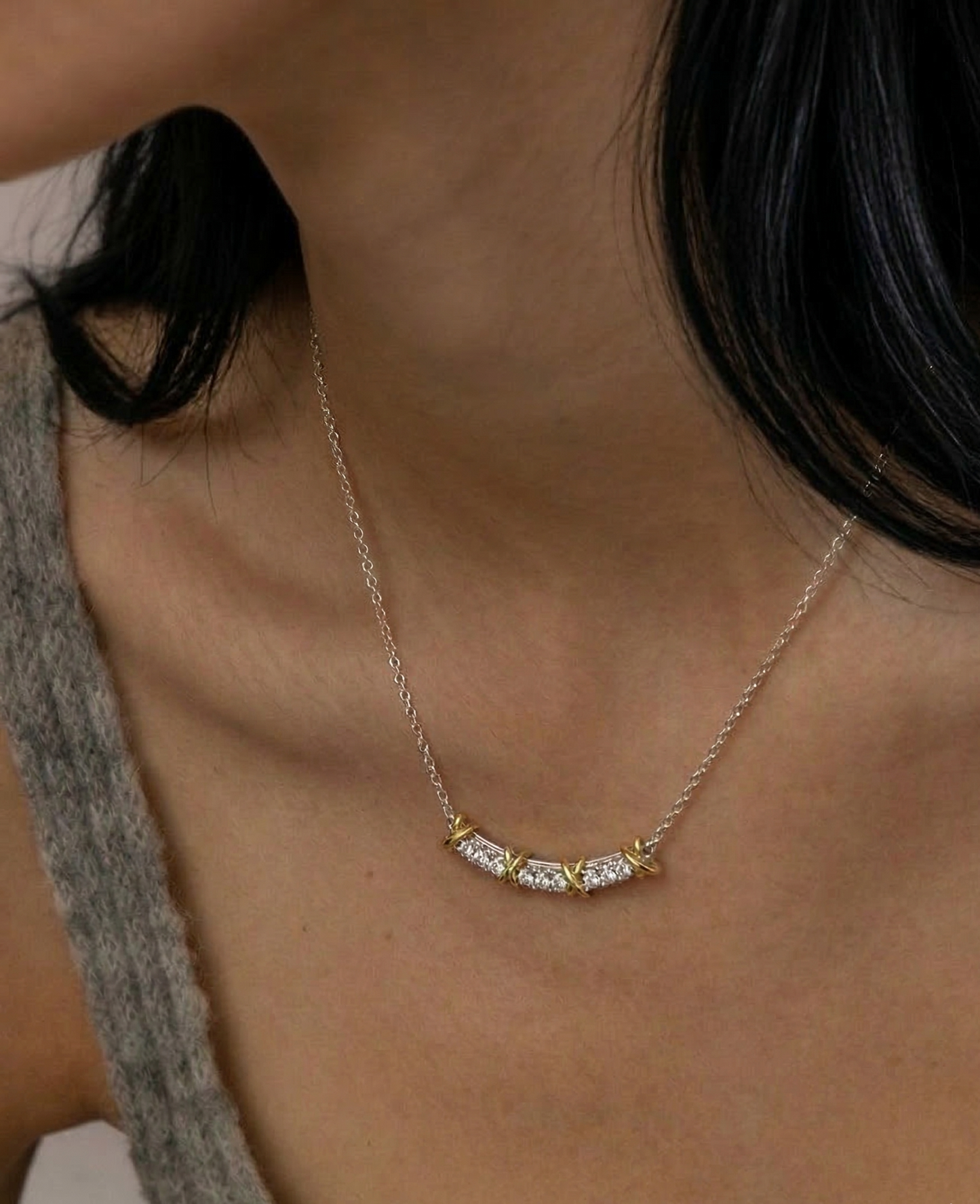 Model wearing silver and gold CZ curved bar necklace with grey knit, collarbone close-up