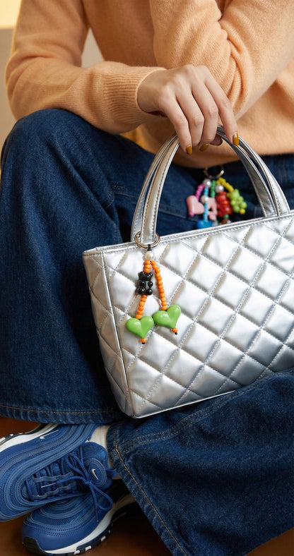 Green and orange double heart beaded bag charm hanging on silver quilted purse with denim outfit