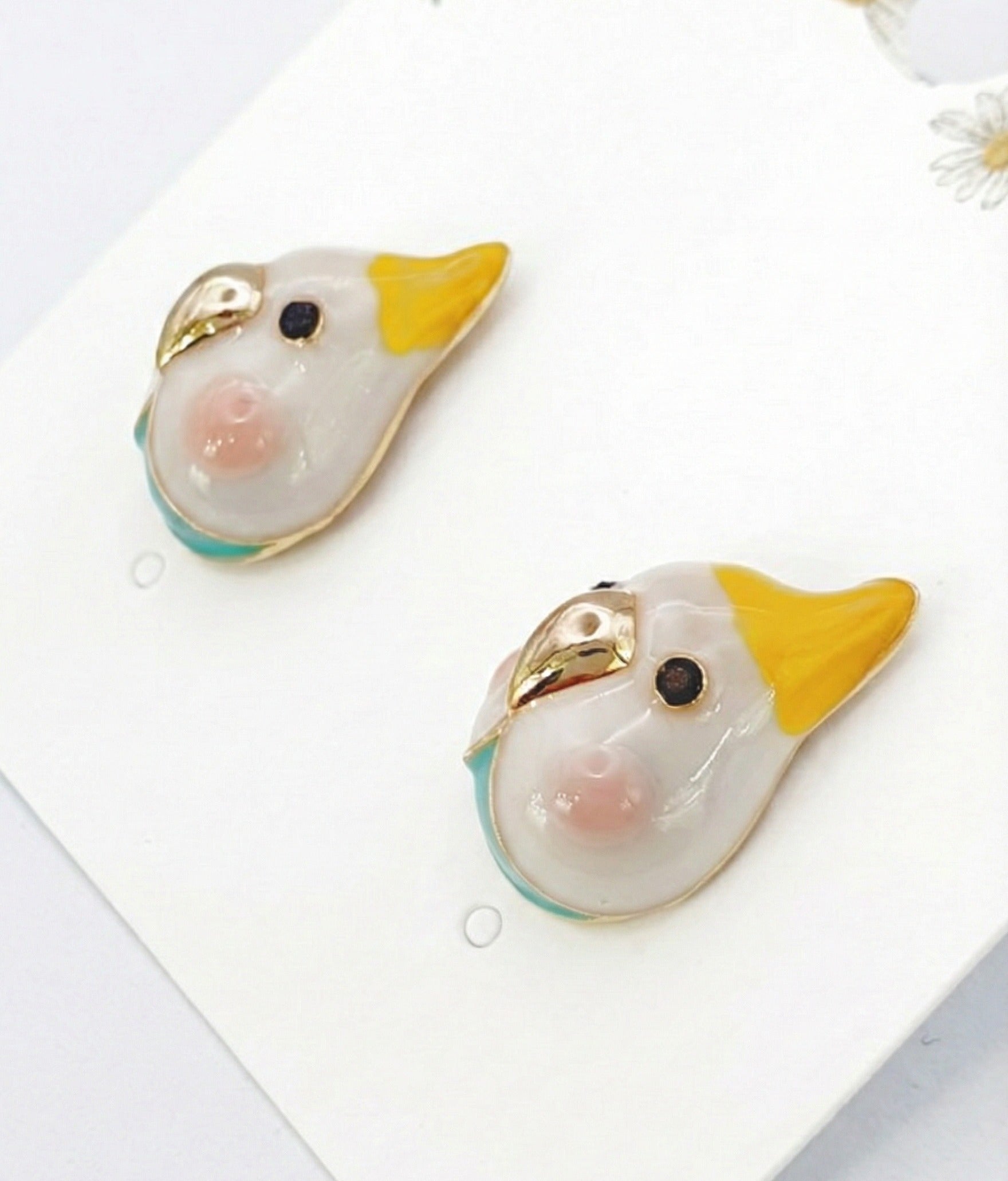  Close-up of white cockatiel earring pair with yellow crest, gold beak and turquoise accent 