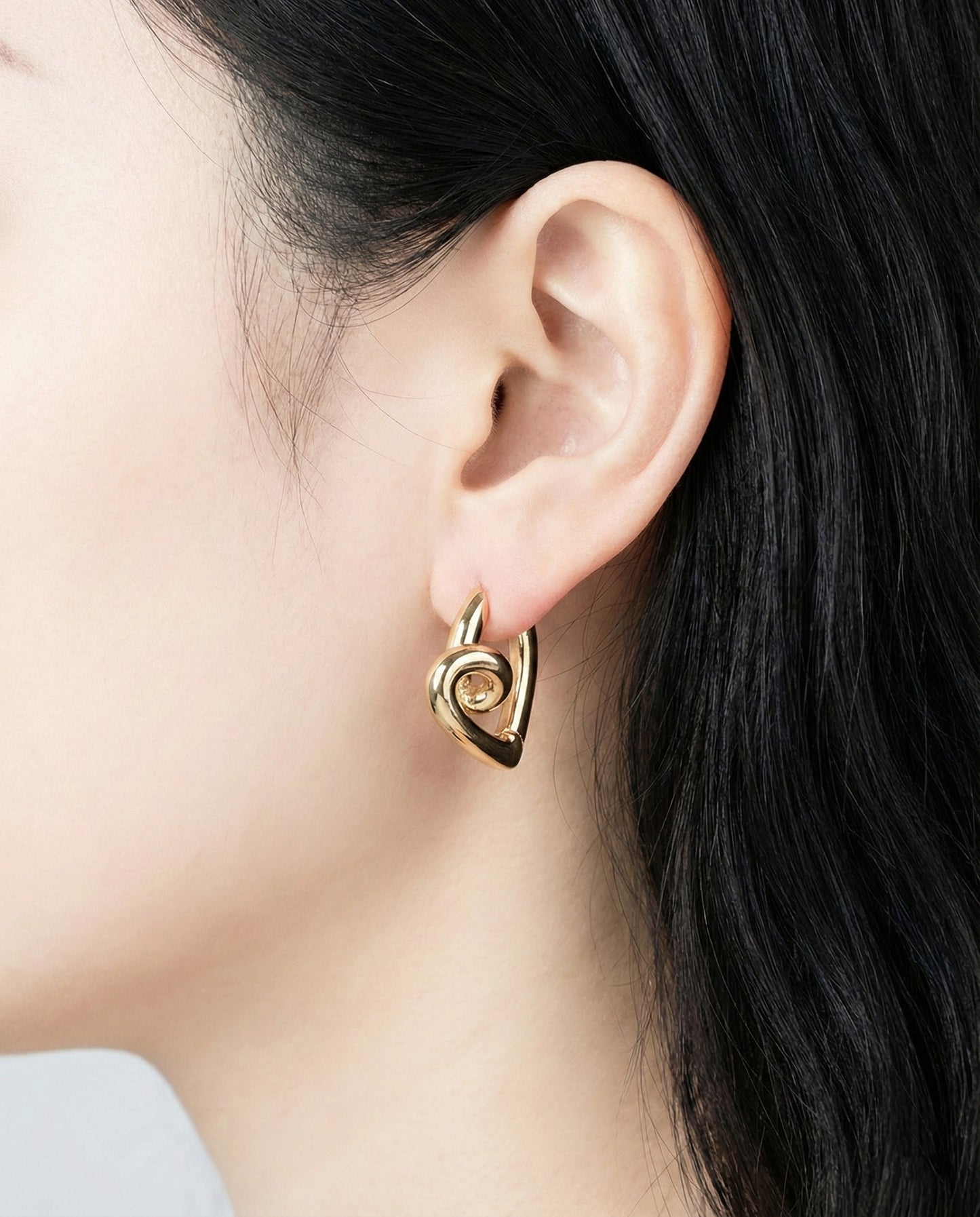 Close-up of gold twisted heart hoop earrings on ear, chunky dimensional knot design jewelry