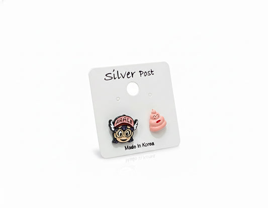Dr. Slump Arale and pink poop character stud earrings displayed on white card with silver posts, Made in Korea label, playful toy background