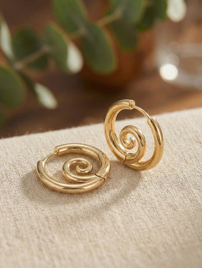 Close-up of gold spiral huggie hoop earrings showing sculptural swirl detail
Silver spiral hoop earrings with inward swirl design on neutral fabric