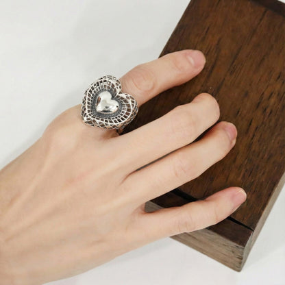 Top view of handmade vintage silver heart ring on wooden surface showing intricate openwork design
