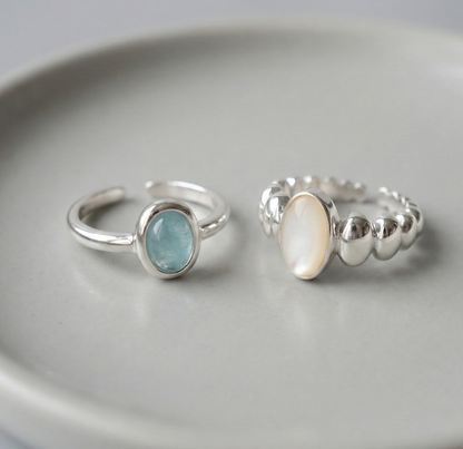 Two 925 sterling silver open rings displayed on white ceramic plate - natural aquamarine ring with smooth band and mother of pearl ring with sculptural ball band side by side