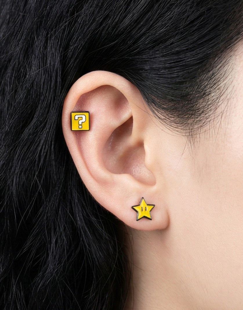 A person wearing mismatched Super Mario-themed earrings: a yellow star stud on the lobe and a yellow question block on the upper ear.