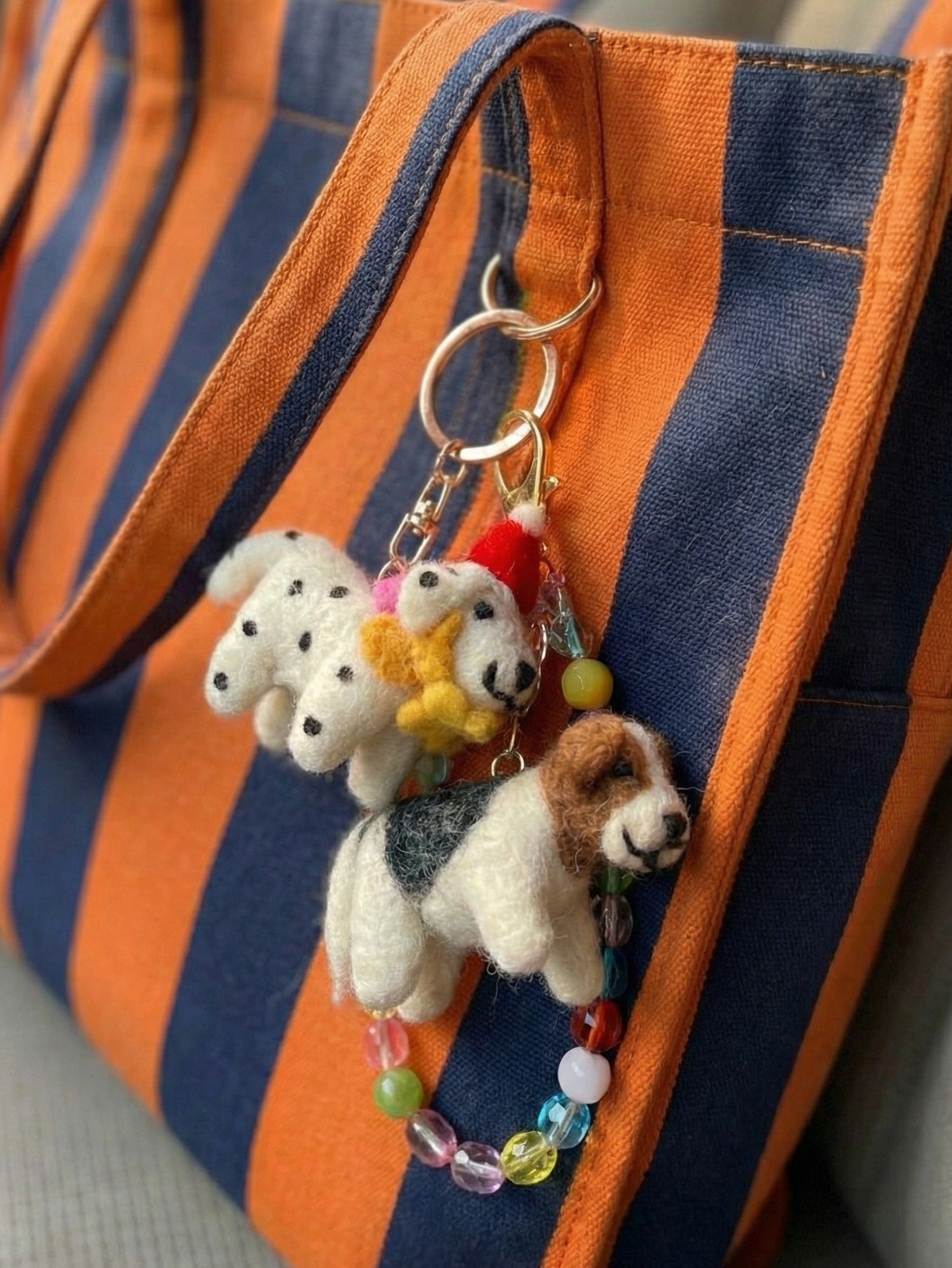 Wool felt dog keychains attached to orange striped backpack strap with colorful bead accents