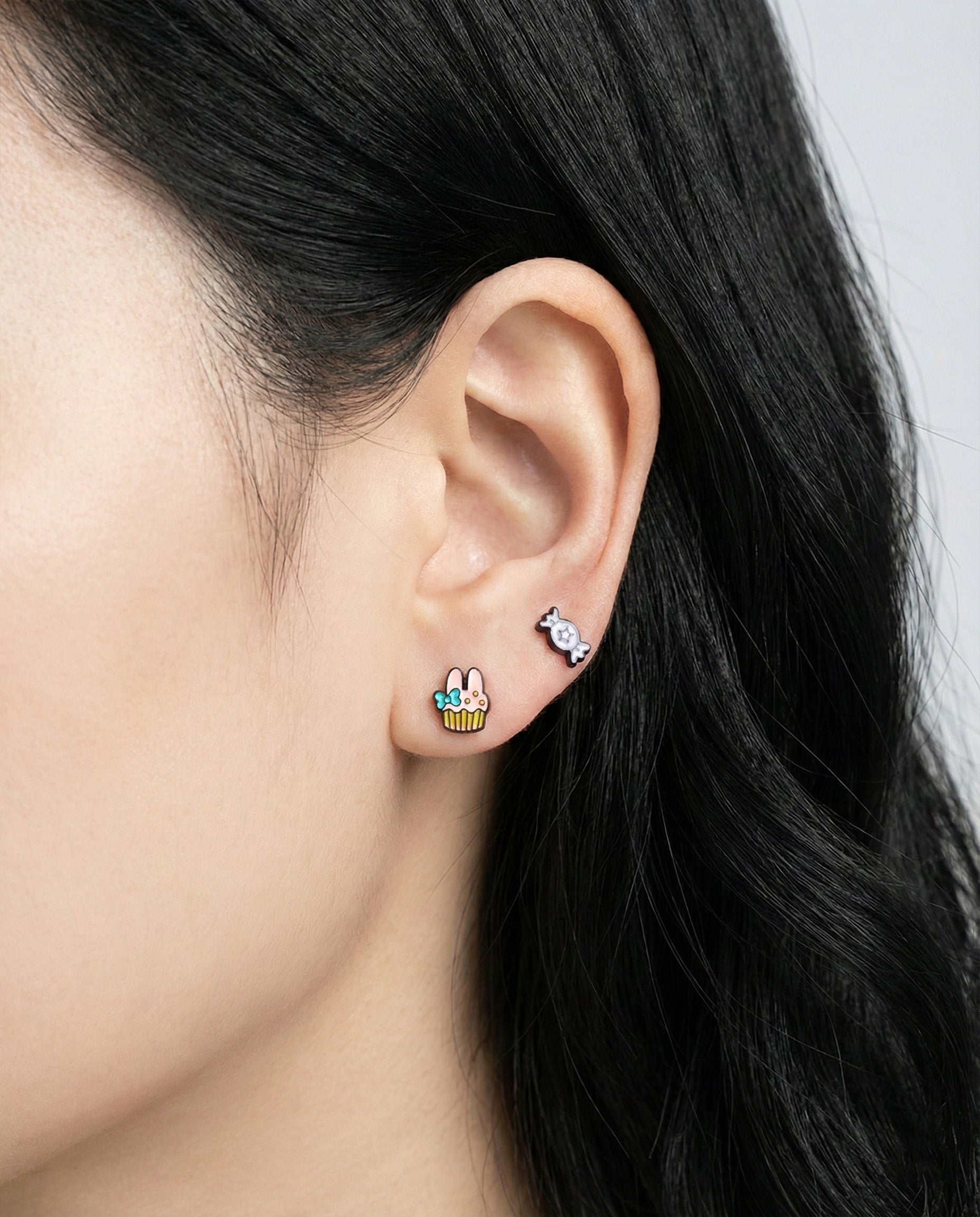 Woman wearing kawaii Sanrio character earrings with cupcake and candy stud earrings layered style