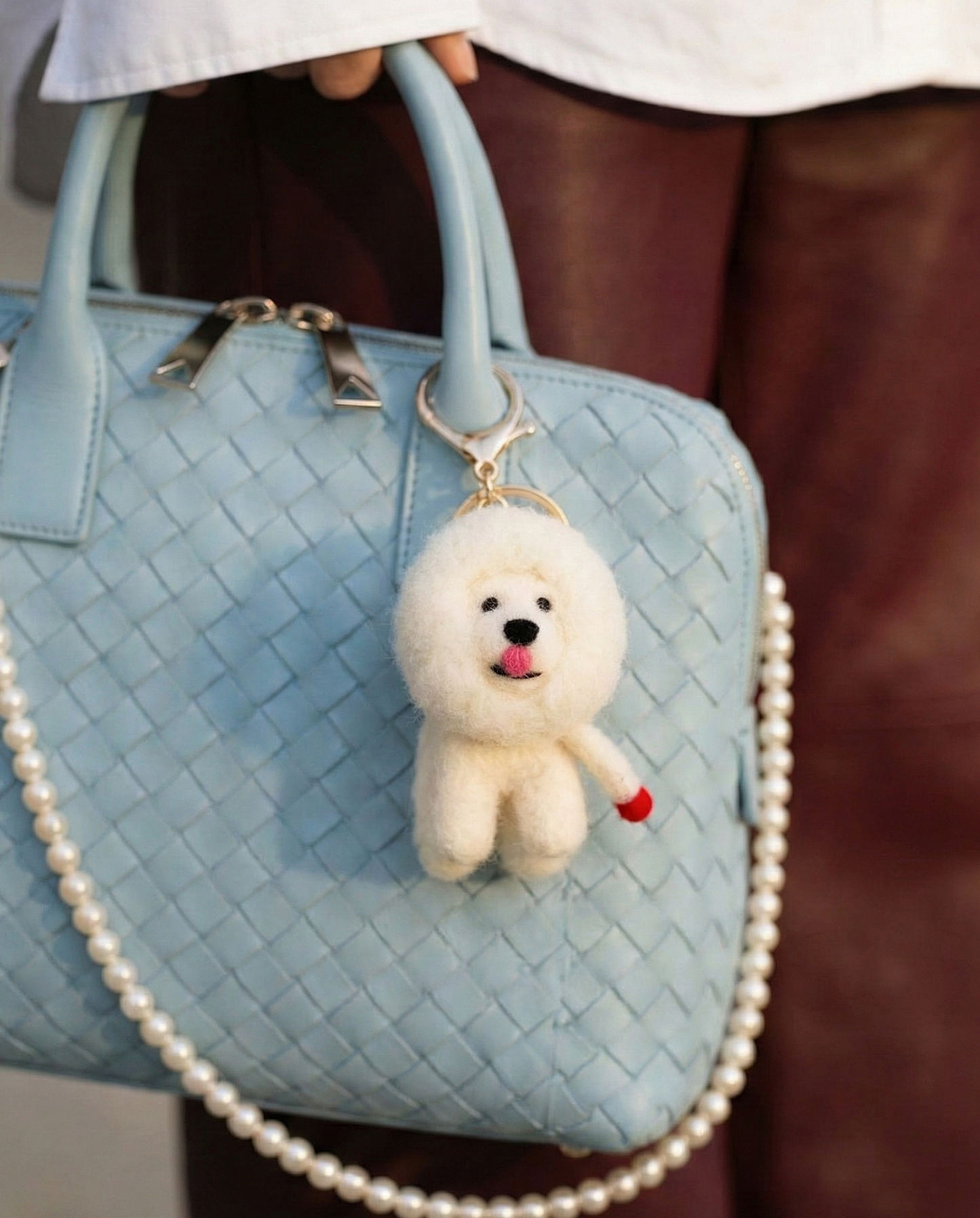 
Fluffy Bichon dog keychain attached to pastel blue woven handbag