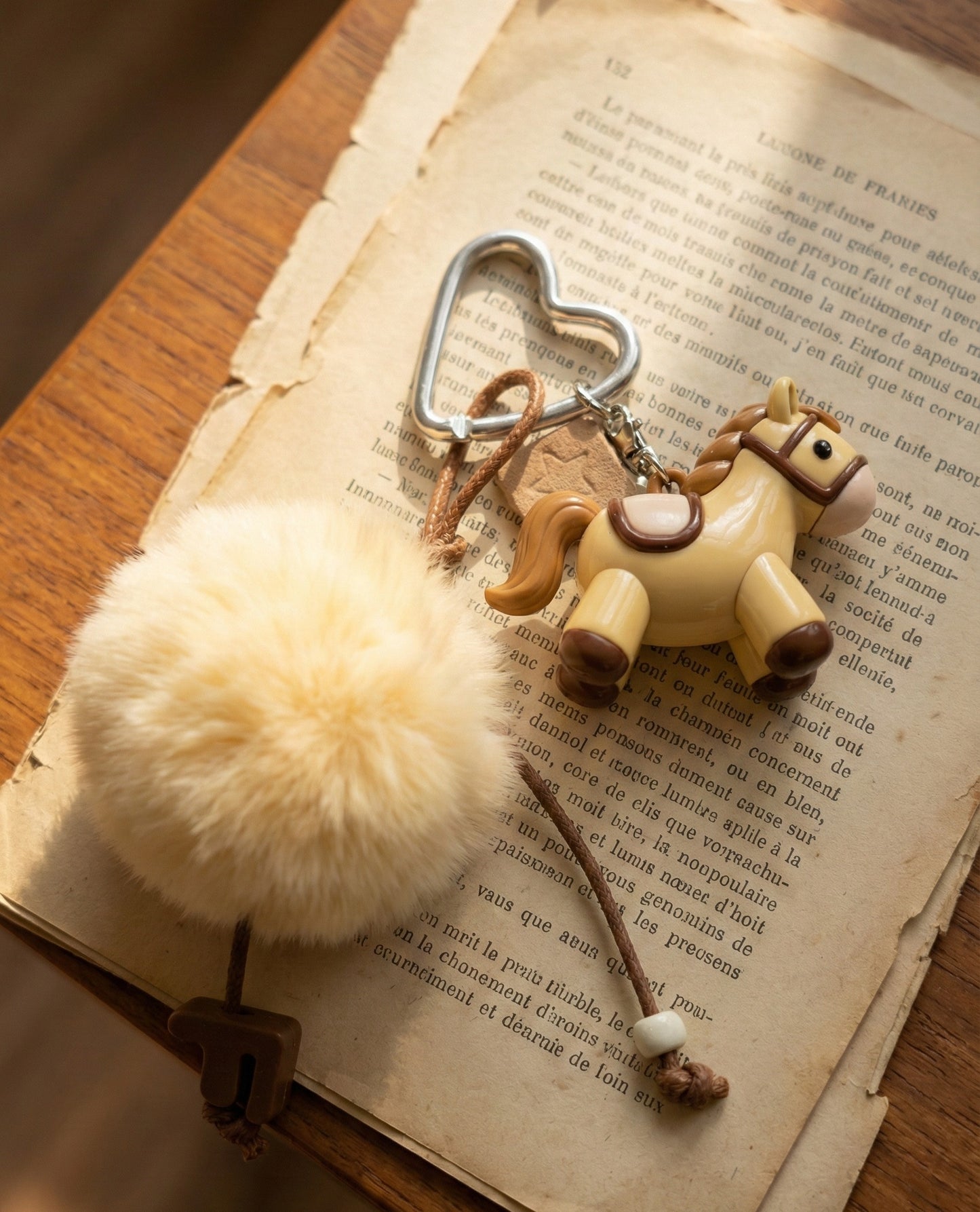 Cream beige pony keychain with heart carabiner and pompom on vintage French book page