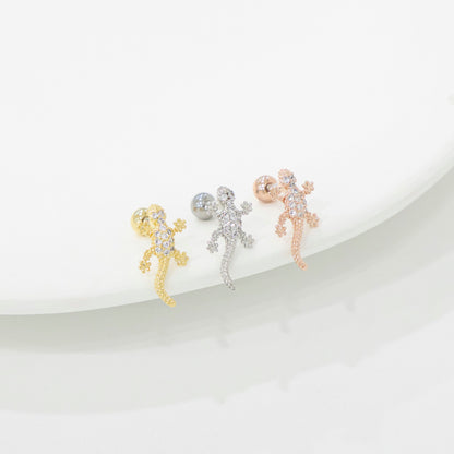 Three gecko-shaped earrings in gold, silver, and rose gold on a white background