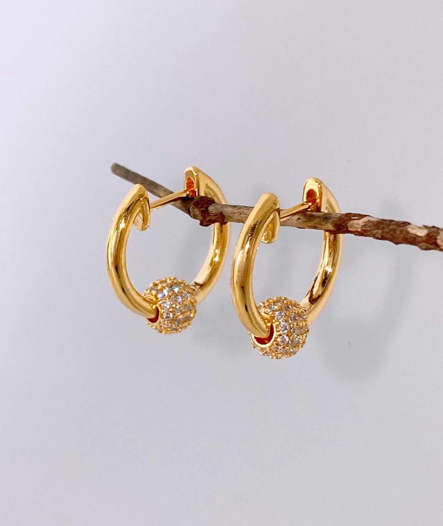 Gold pave ball huggie hoop earrings on natural branch close-up view