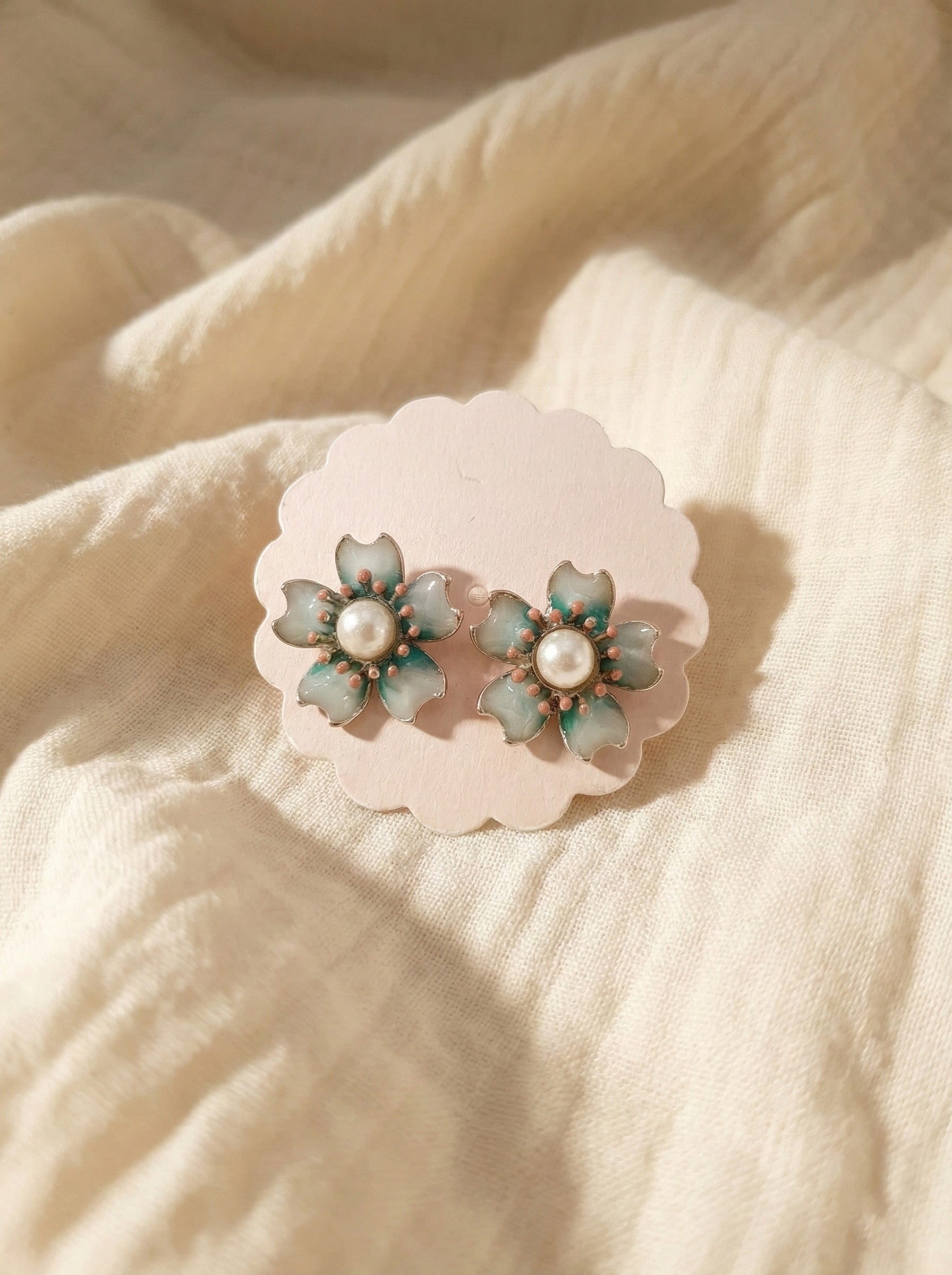 Close-up of jade mint enamel flower earrings with pearl center and watercolor gradient effect on scalloped paper card