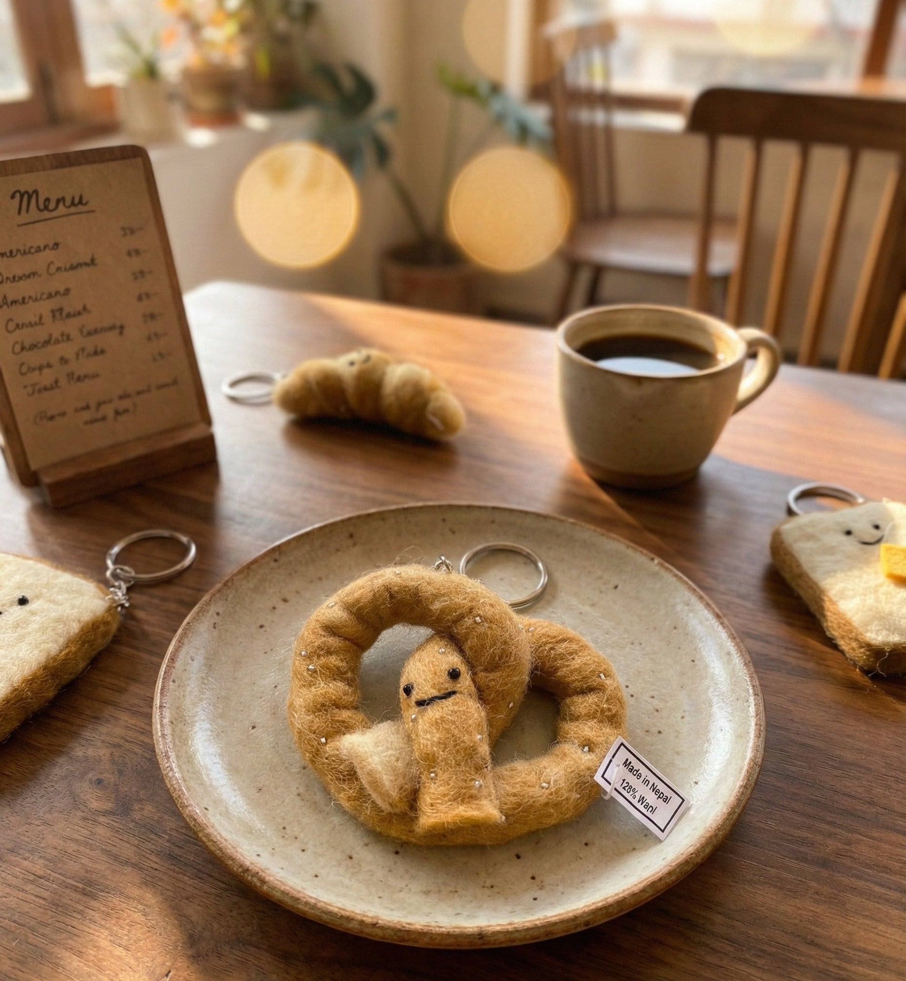 Close-up of handmade Nepal wool felt pretzel keychain on plate with Made in Nepal tag