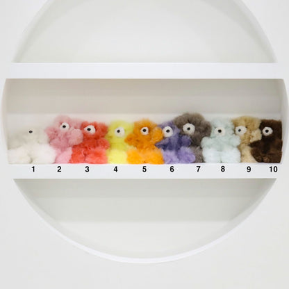 Ten alpaca bear keychains numbered 1 to 10 displayed on a white shelf in a circular frame, showing full color lineup from white, pink, coral, yellow-green, orange, purple, gray, mint, beige to brown