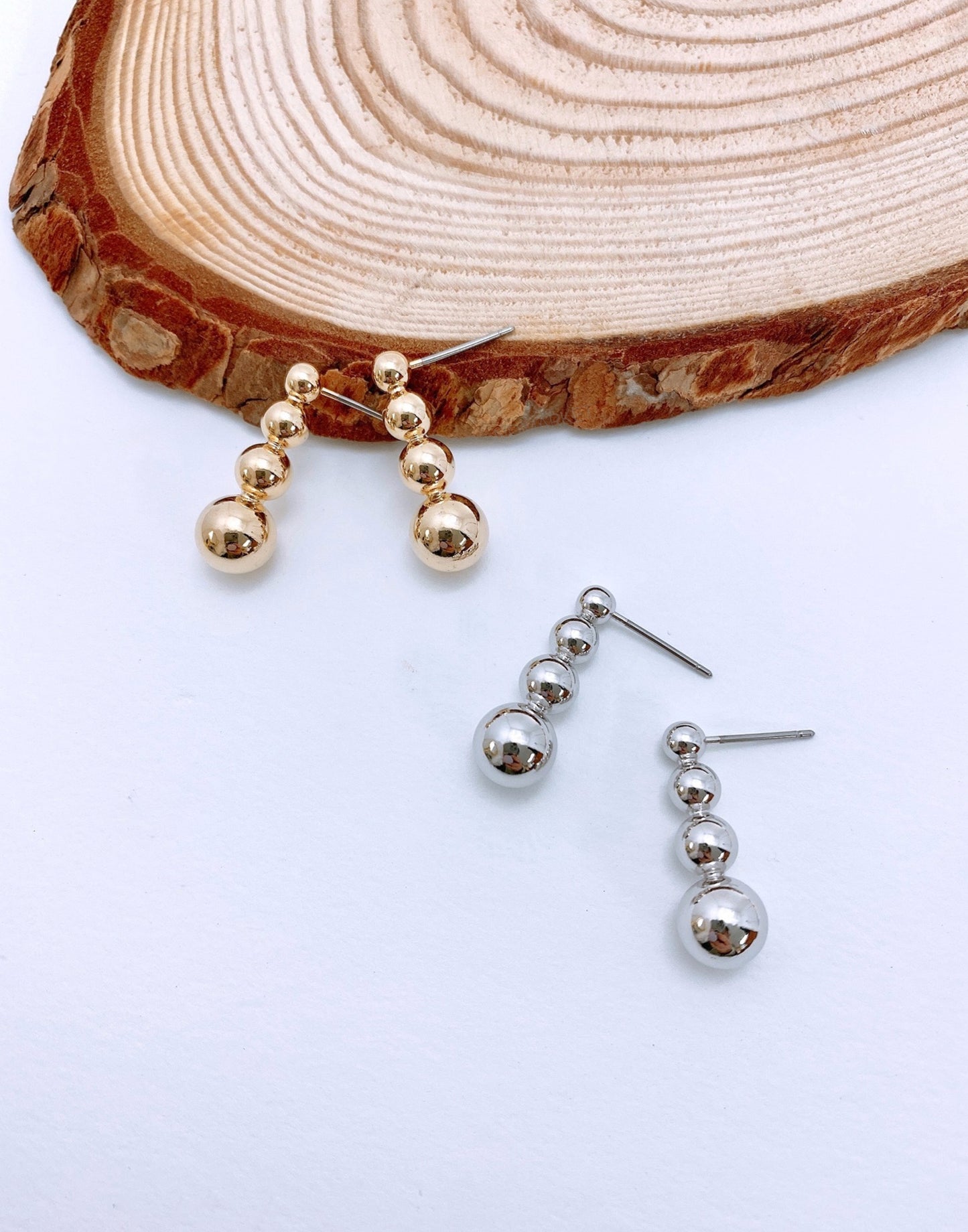Gold and silver 4-tier graduated sphere bar stud earrings on wood slice display