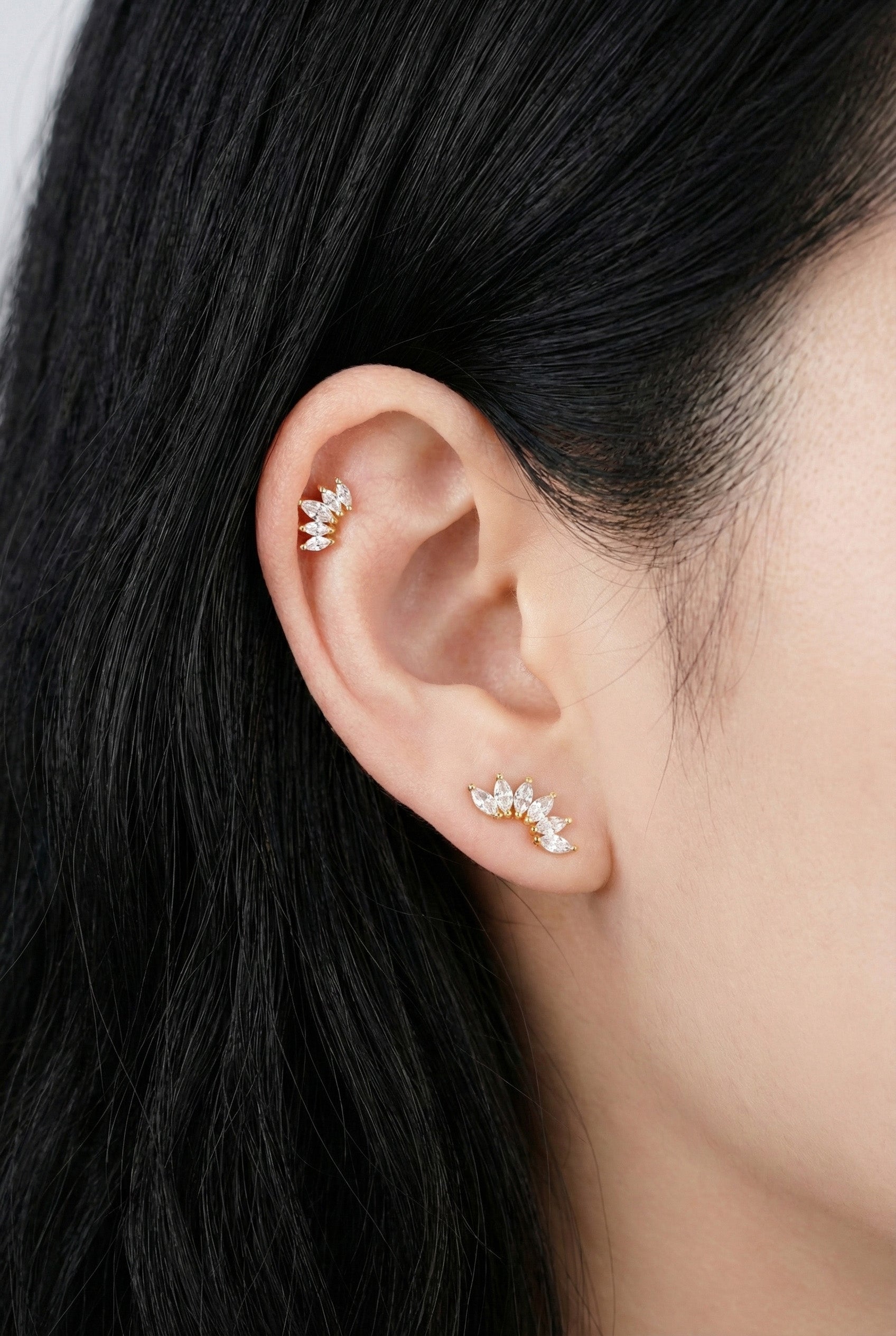 Model wearing curved wing marquise cubic cartilage piercing on helix with layered earrings