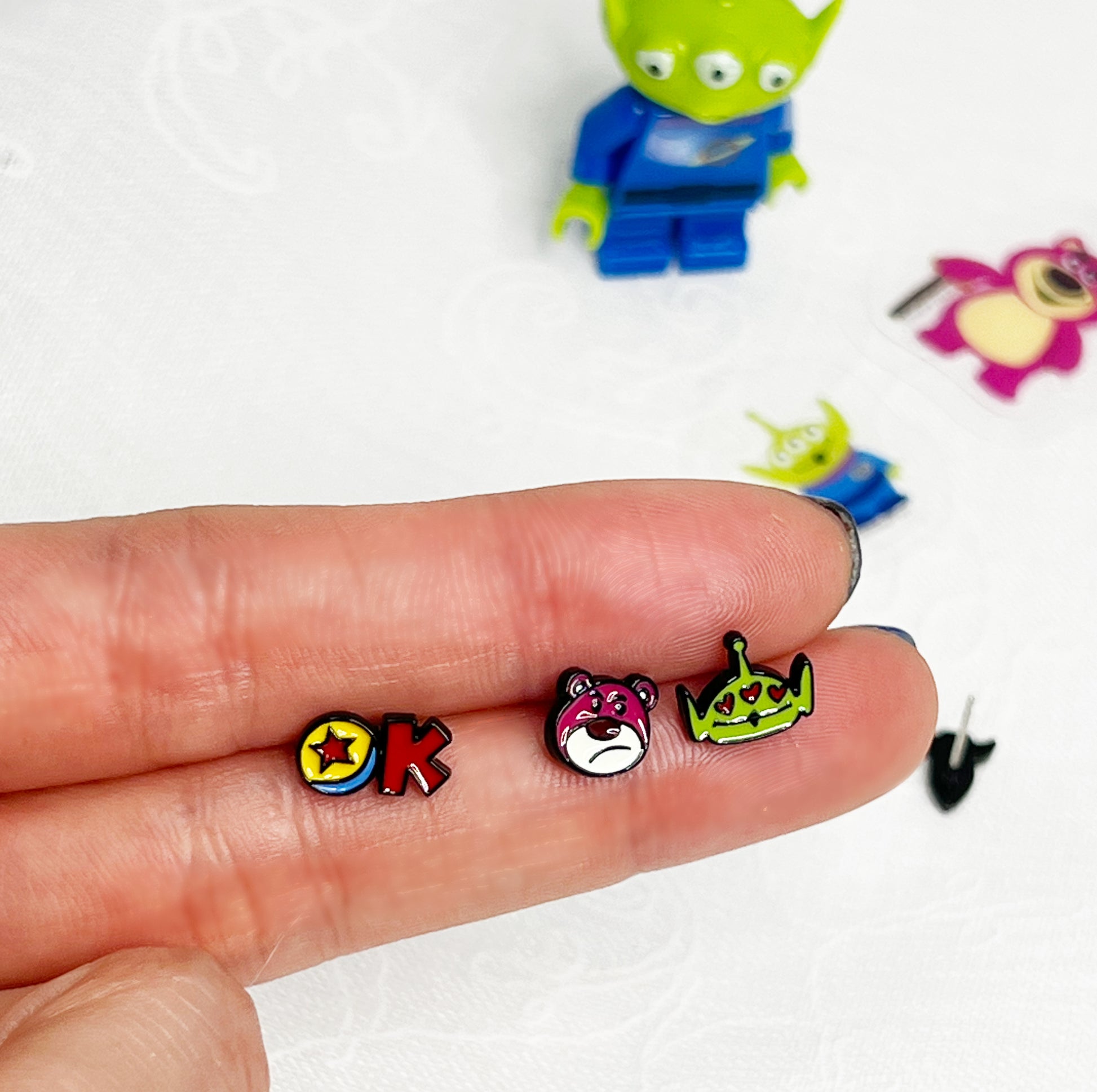 Close-up of mini Toy Story character earrings held in hand showing size and vibrant enamel details